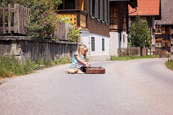 Kind mit Schultasche sitzt auf einer ruhigen Straße zwischen Häusern.