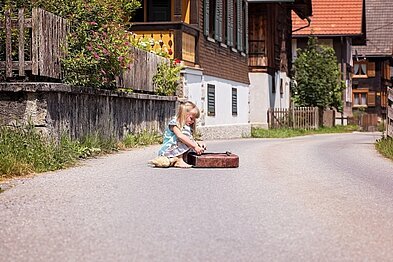Kind sitzt mit Schultasche auf der Straße 